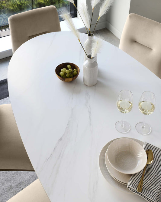 A sleek oval dining table adorned with elegant tableware, glasses of wine, and decorative vases, set with soft beige chairs.