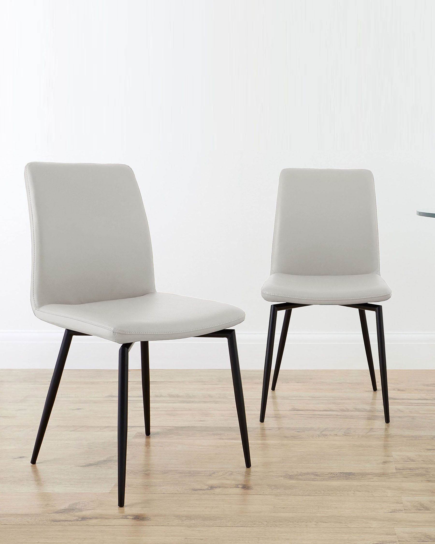 Two minimalist gray dining chairs with sleek black legs, set against a light background and wooden floor.