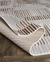 Modern striped area rug in neutral tones partly rolled up on a hardwood floor.