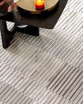 A contemporary round black coffee table with a thick tabletop and cylindrical legs on a modern patterned area rug featuring a geometric stripe design in shades of grey and beige.