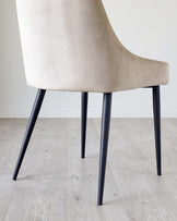 A sleek beige upholstered chair with a low back and stylish black metal legs, perfect for modern interiors.