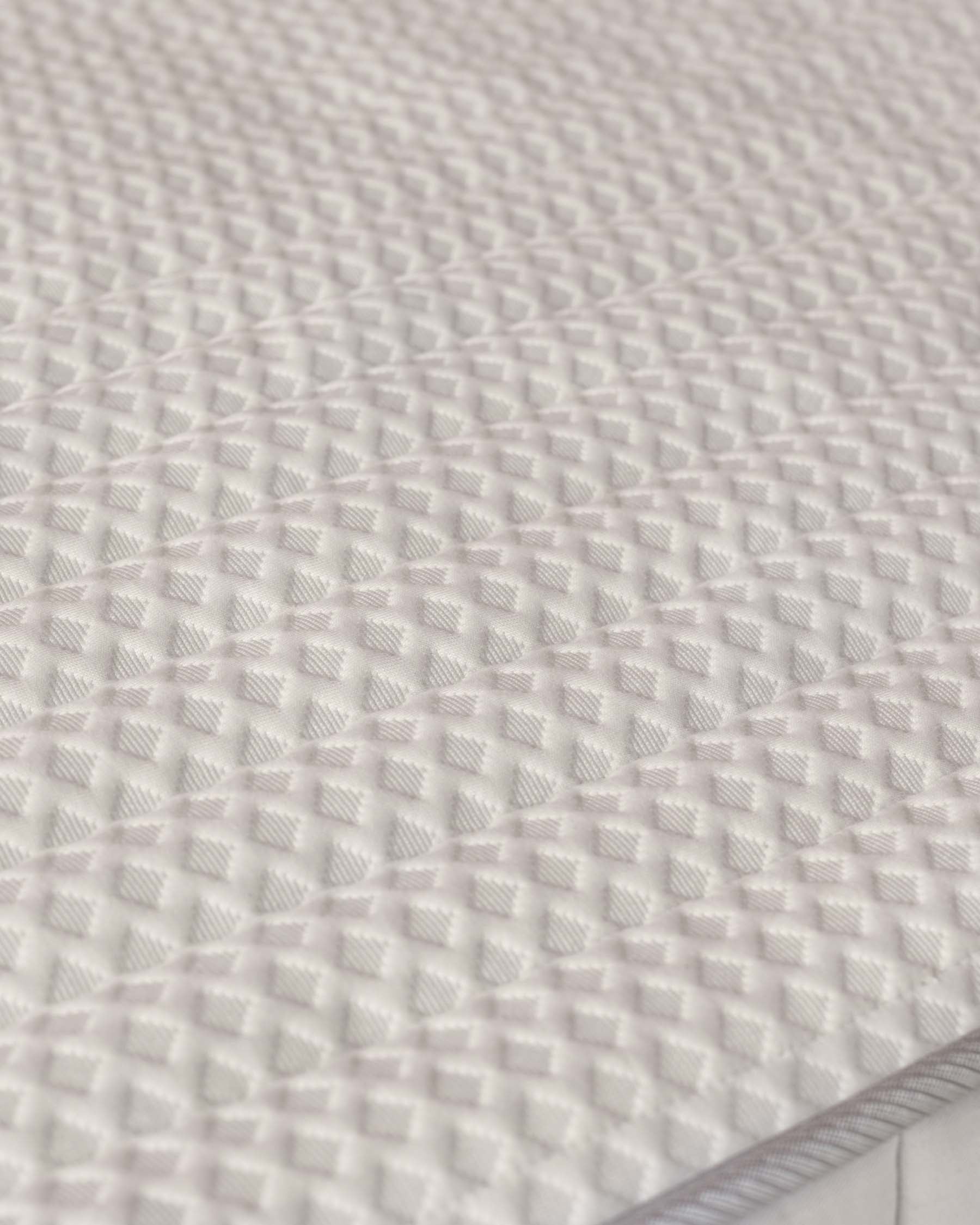 Close-up of a textured, white mattress featuring a diamond-patterned surface for comfort and support.