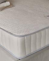 Close-up of a quilted mattress with a textured surface and plush side panel resting on a soft bed frame.