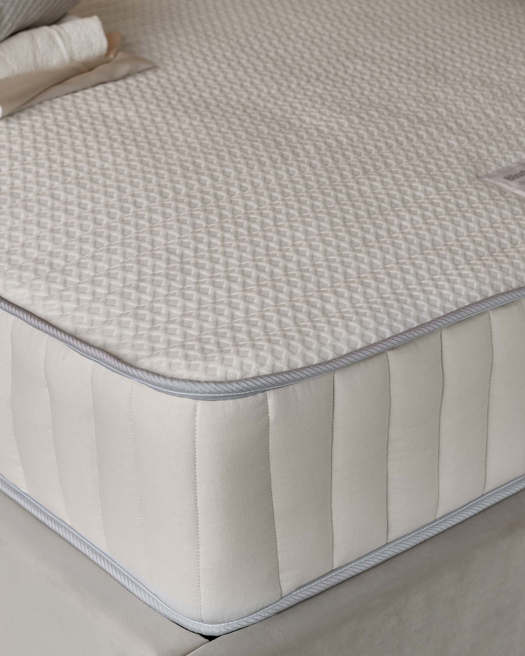 Plush, quilted mattress with textured surface and soft, padded edges, set atop a light-colored upholstered base.