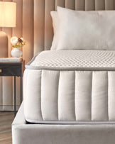 A plush mattress with a soft quilted surface rests on a sleek upholstered bed frame, accompanied by a stylish bedside lamp and décor.