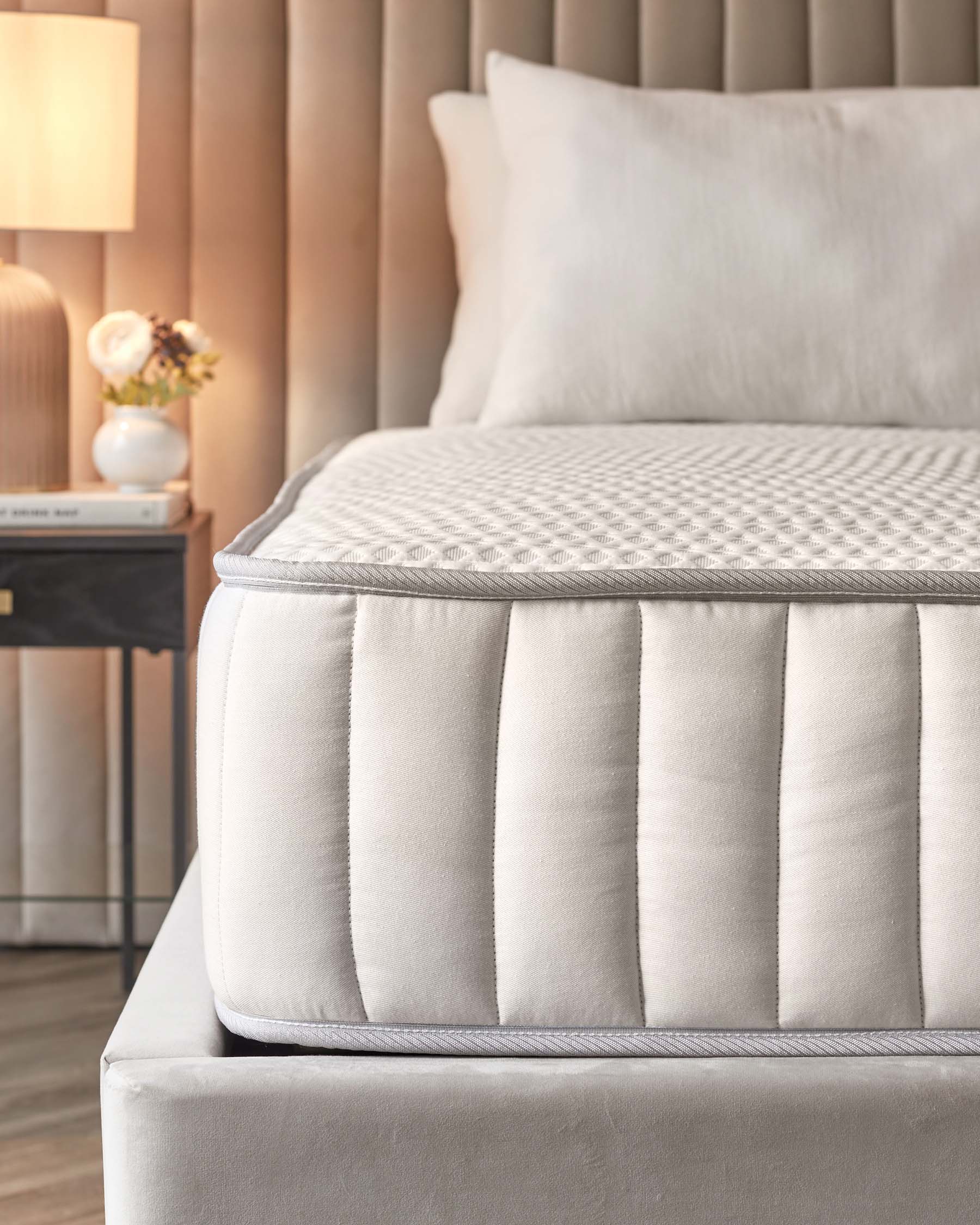 A plush mattress atop a stylish bed frame, with soft pillows and a contemporary nightstand featuring a lamp and flowers.