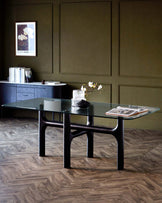 A modern glass dining table with black sculptural legs, paired with a stylish sideboard and elegant decor.