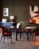 A modern dining set with a glass table and plush, terracotta-colored chairs, complemented by stylish decor and lighting.