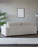 Modern three-seater fabric sofa in a neutral beige colour with plush cushions, clean lines, and wooden legs, positioned on a contemporary two-tone area rug.