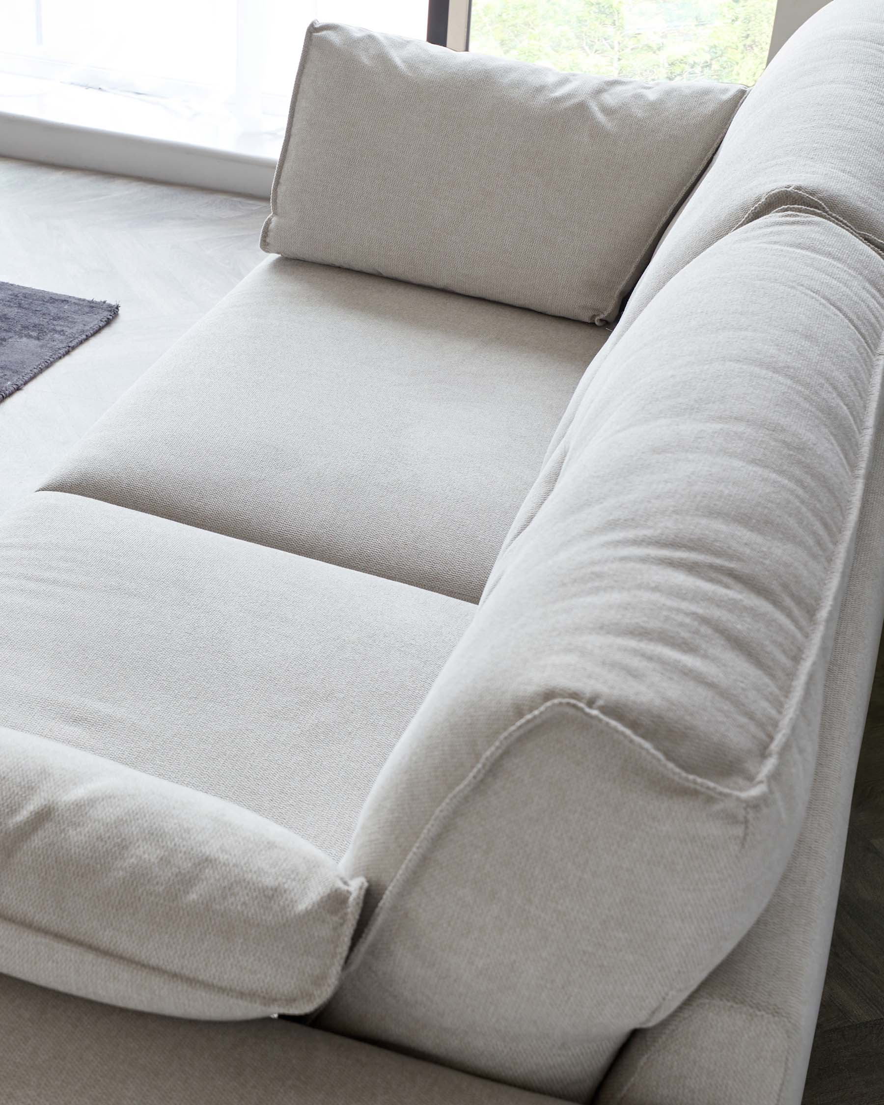 Close-up of a contemporary light grey fabric sofa featuring plush cushions, a softly padded armrest, and a comfortable, inviting seat.