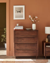 Modern wood dresser with three drawers, a paired nightstand, a decorative vase, framed art, and stacked books.