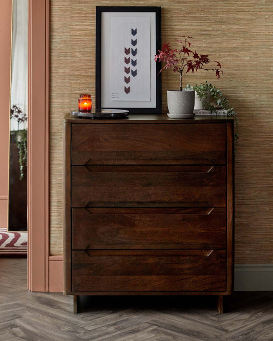 Stylish wooden chest of drawers with four spacious drawers, decorated with a small plant, framed art, and a candle on top.