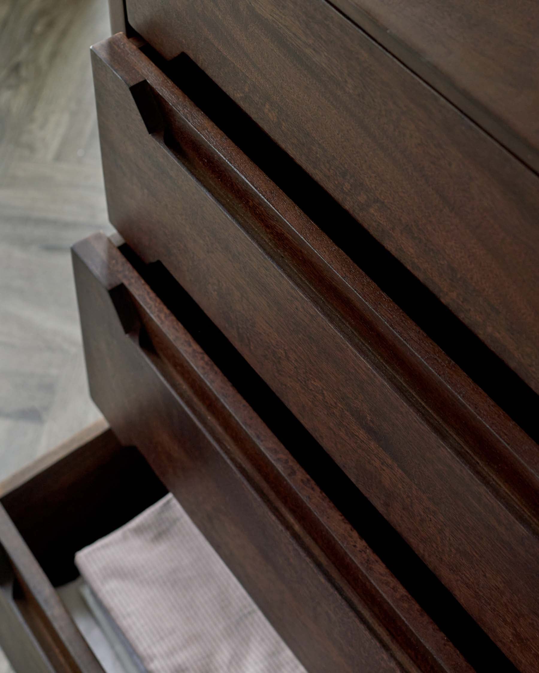 Close-up of a dark wood dresser featuring sleek, minimalist drawer pulls and an open drawer with neatly folded fabric.