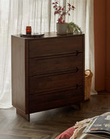 A dark wood chest of drawers with three spacious drawers, topped with a round tray, a candle, and potted plants.