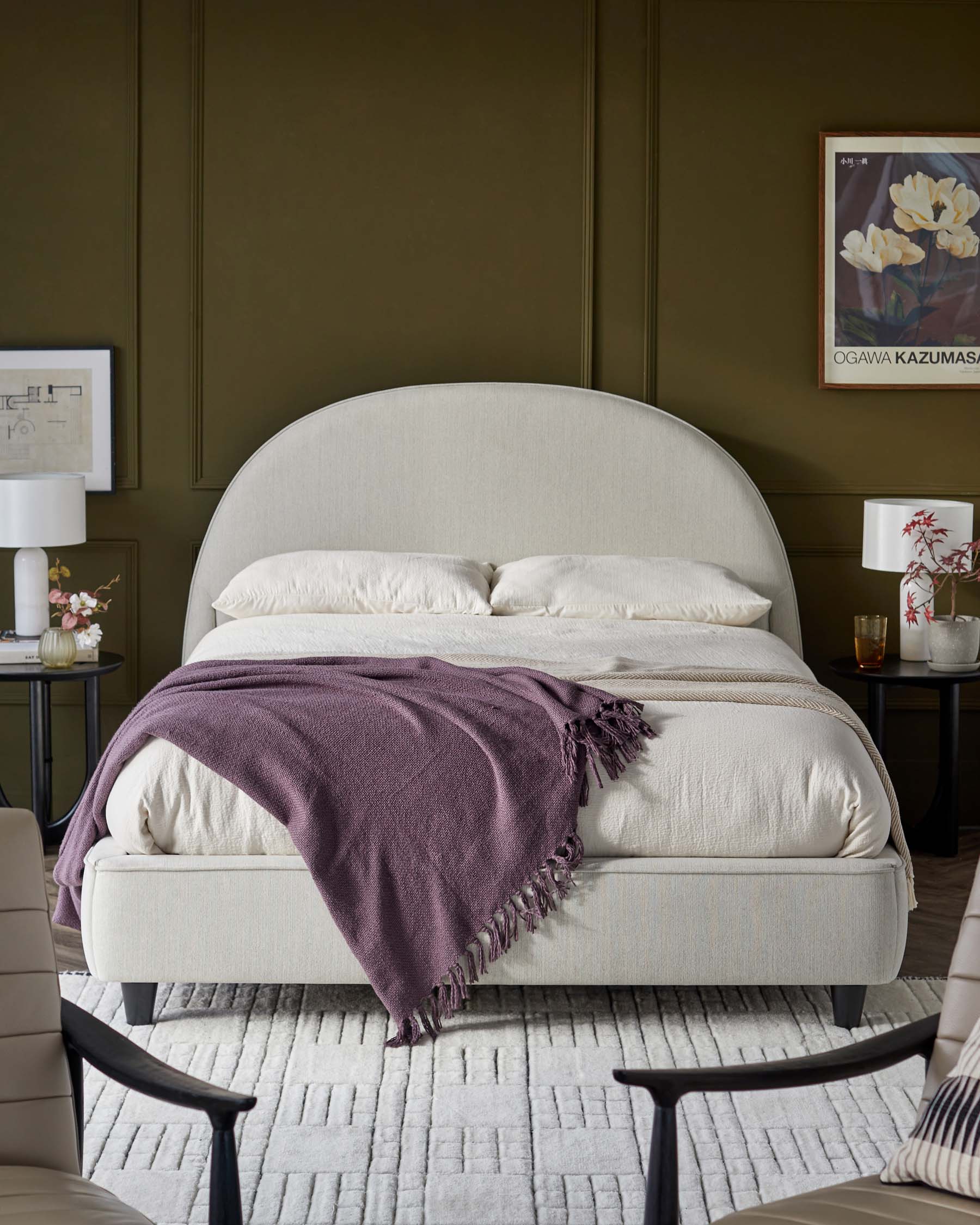 A plush bed with a curved headboard, layered in neutral tones, accompanied by nightstands, table lamps, and a cozy throw.