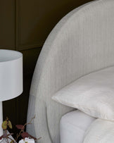 Elegant upholstered bed with a curved headboard, paired with a simple white lamp and soft, textured bedding.