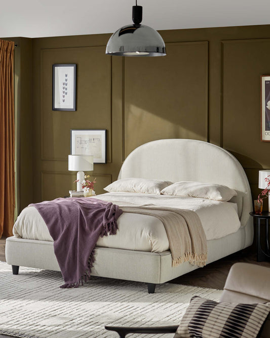 Stylish upholstered bed with curved headboard, layered throws, modern lighting, and accent decor in a cozy, chic setting.