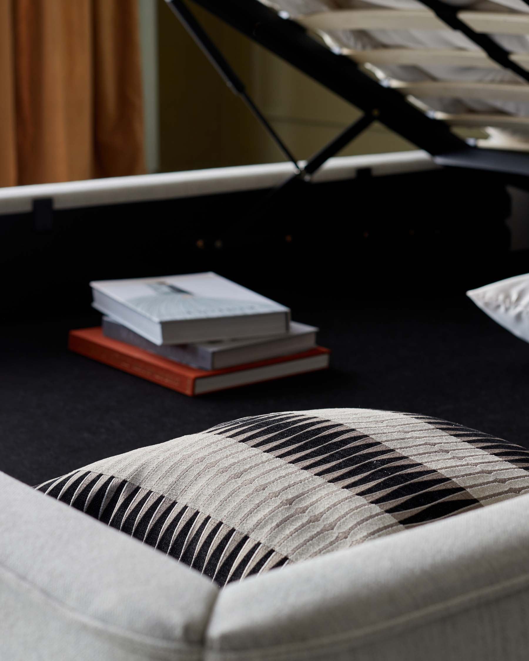 A cozy upholstered sofa with a patterned cushion, featuring stacked books on a black surface beneath a raised mattress.