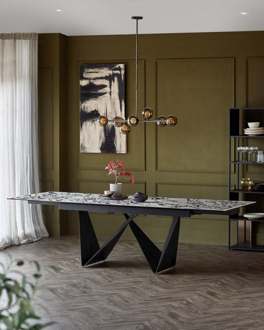 A modern black dining table with a marble top and striking angular legs, paired with a contemporary pendant light above.