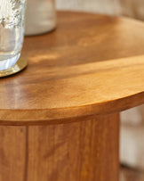 A close-up of a round, wooden table surface featuring a smooth finish and warm tones, complemented by a glass and coasters.