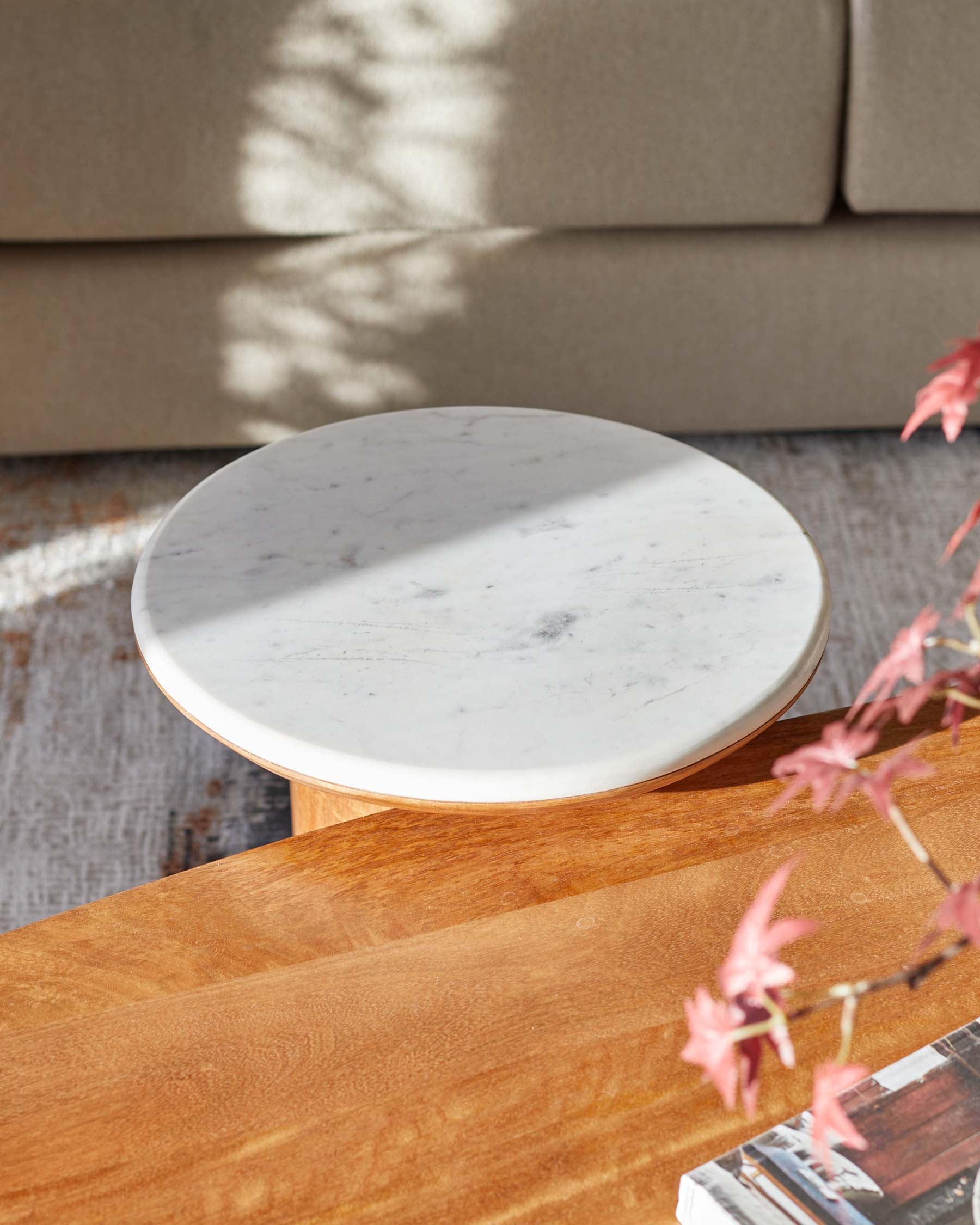 Round marble-topped side table with a wooden base, set against a neutral backdrop with soft natural lighting.