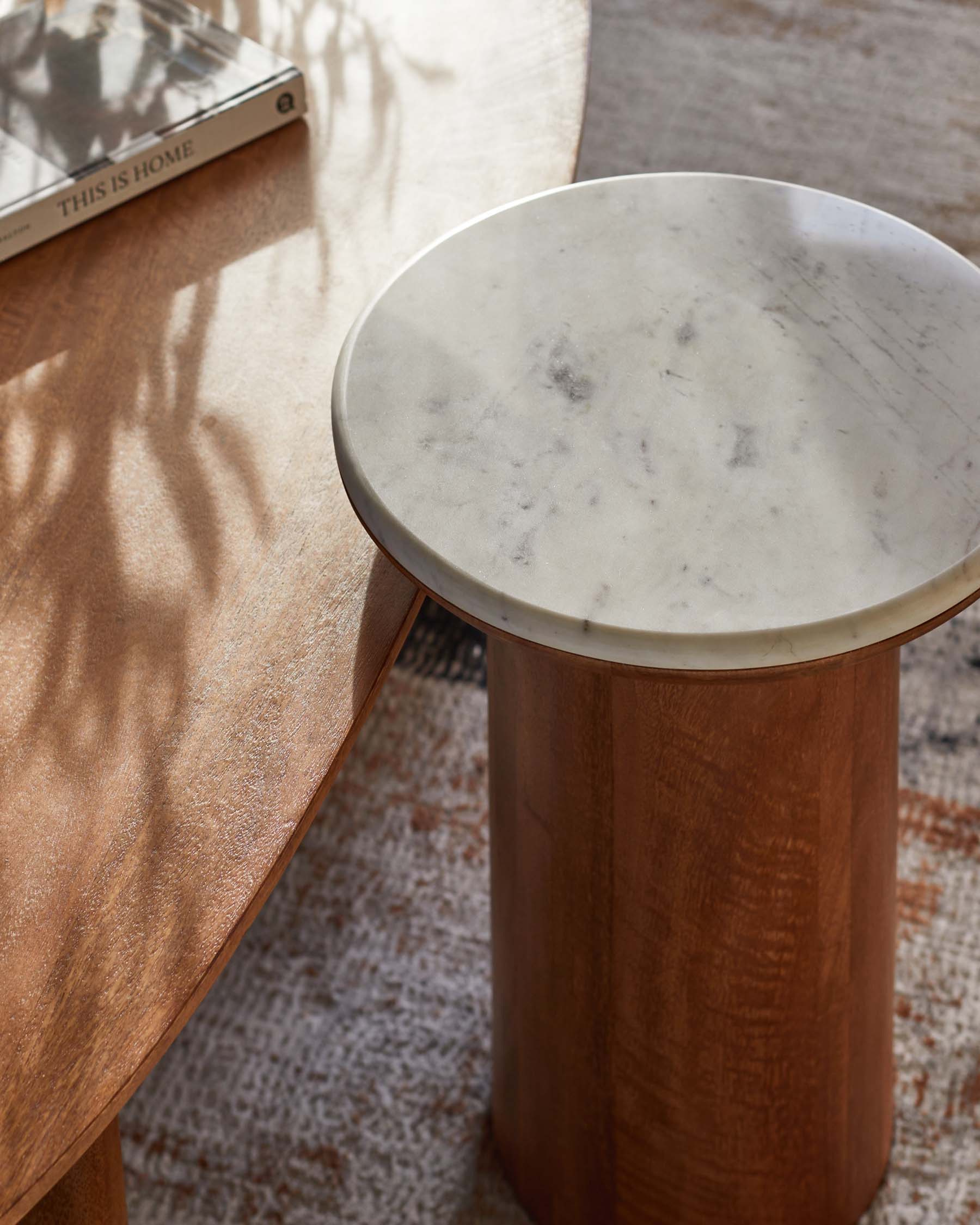 A round marble-topped side table stands beside a curved wooden coffee table, both on a textured area rug.