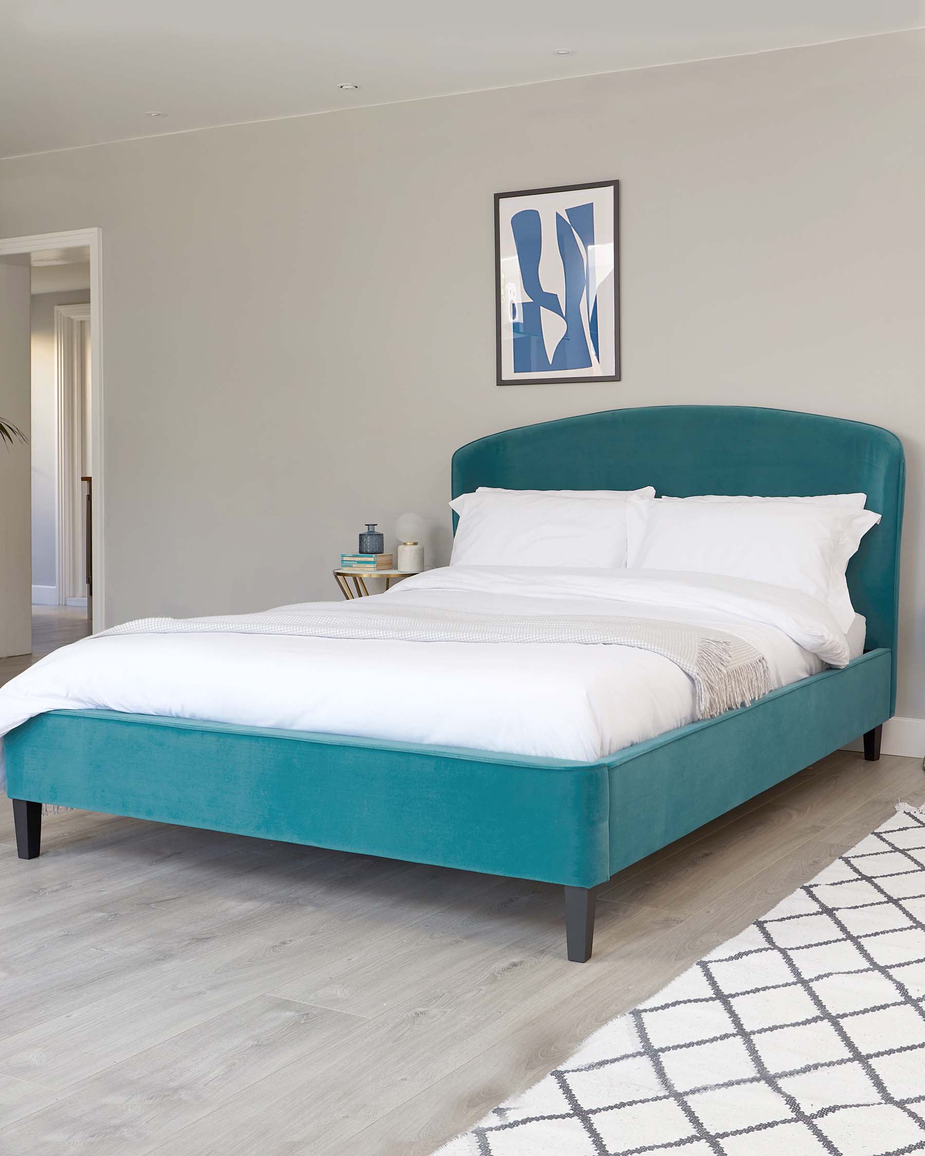 Teal upholstered bed with a rounded headboard, white bedding, and a stylish bedside table set against a neutral wall.