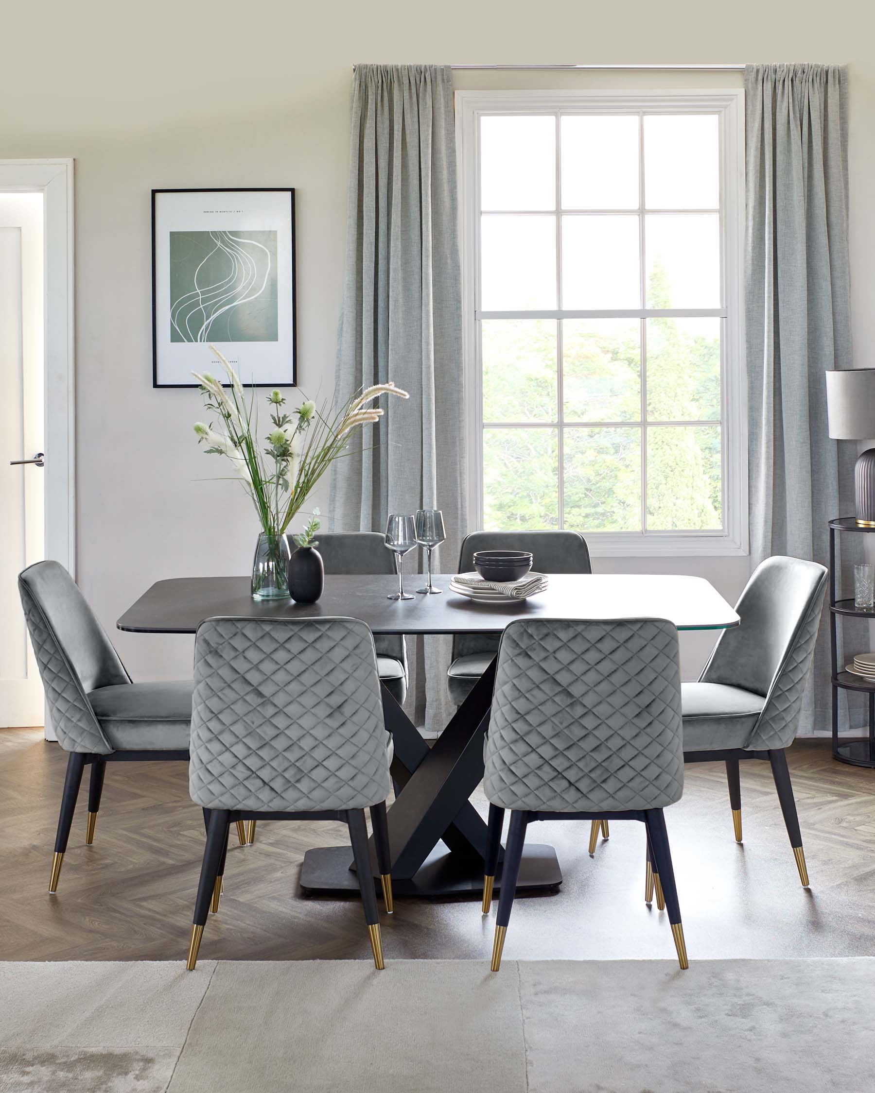 Modern dining set featuring a sleek, gray rectangular table and four quilted velvet chairs with gold-tipped legs.