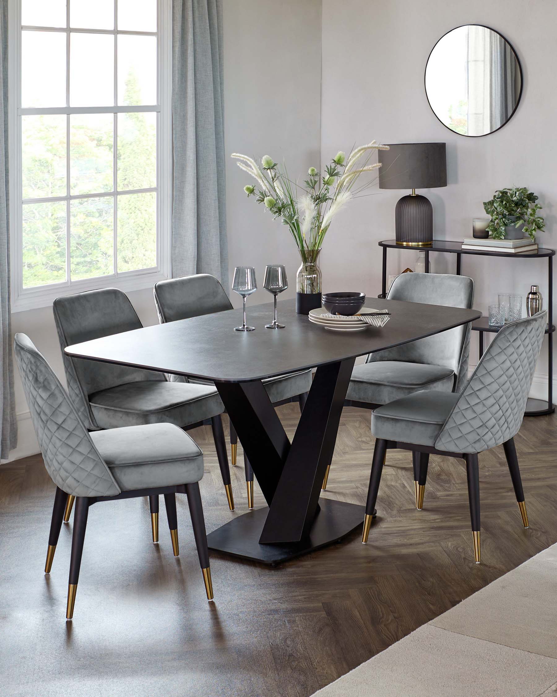 Modern dining set featuring a stylish black table with a unique base and plush grey upholstered chairs with gold accents.