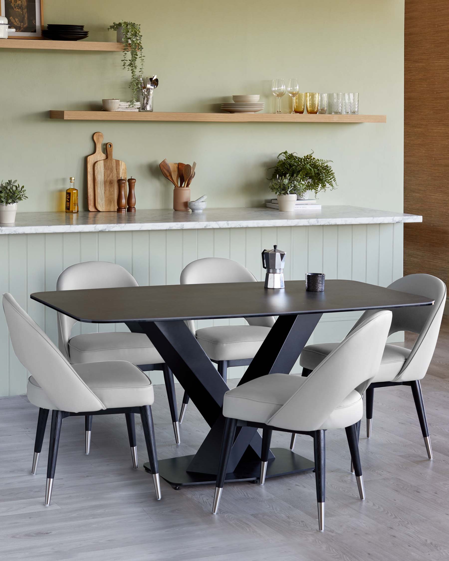 A contemporary dining set featuring a rectangular table with a matte black top and a sculptural X-shaped base in a contrasting dark finish. Accompanied by four sleek chairs upholstered in light grey fabric with tapered black legs tipped with metallic accents.