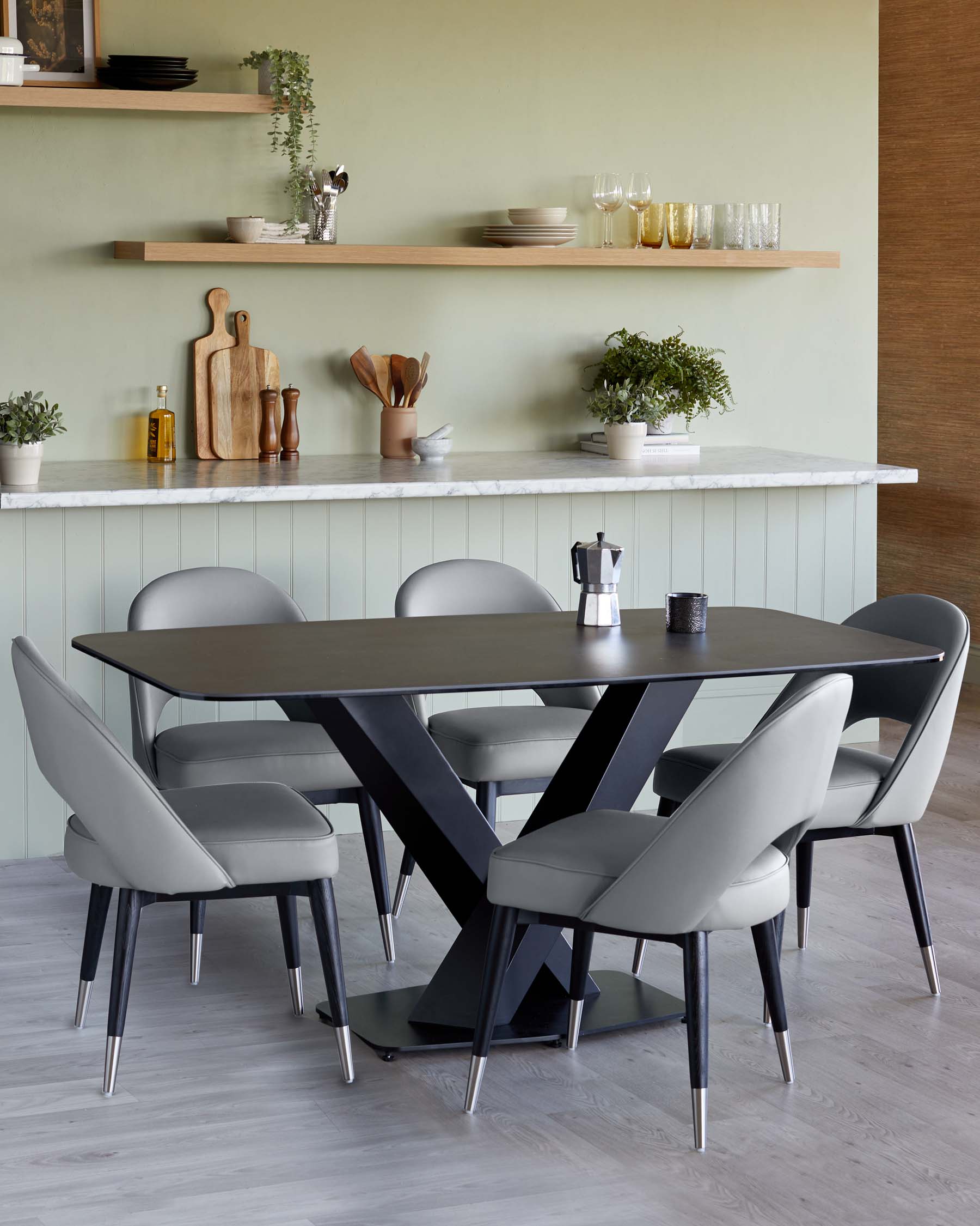 Modern dining set featuring a dark grey oval table with intersecting black metal legs and a set of six sleek grey upholstered dining chairs with black metal legs tipped with metallic accents.