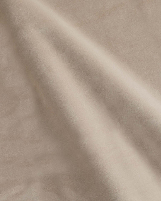 Luxurious, smooth beige upholstery fabric displaying gentle folds, ideal for elegant furniture pieces.