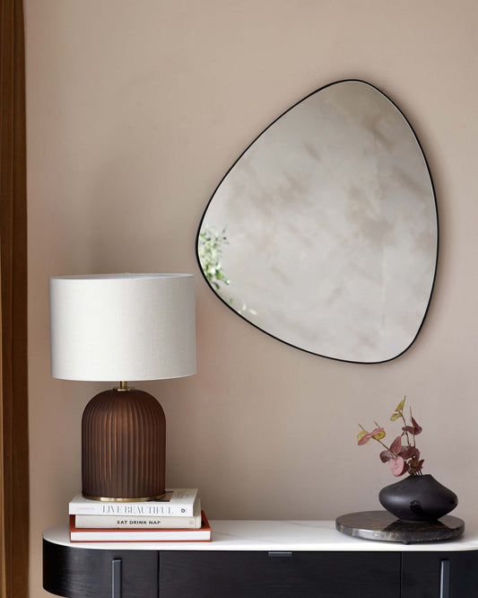 Modern minimalist console table in black with a smooth finish, sleek rectangular form, and subtly rounded corners. On the tabletop, there is a contemporary ribbed table lamp with a white shade and a stack of books, beside which sits an artistic vase with delicate flowers.