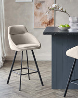 Modern bar stool with a beige upholstery seat and backrest, featuring sleek black metal legs and a geometric footrest.