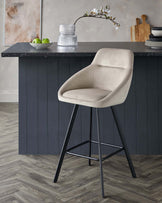 Modern bar stool with beige upholstered seat and backrest, featuring sleek black metal legs with footrest.