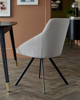 Stylish gray upholstered chair with a sculpted backrest and black metal legs, paired with a wooden table, set in a modern interior.