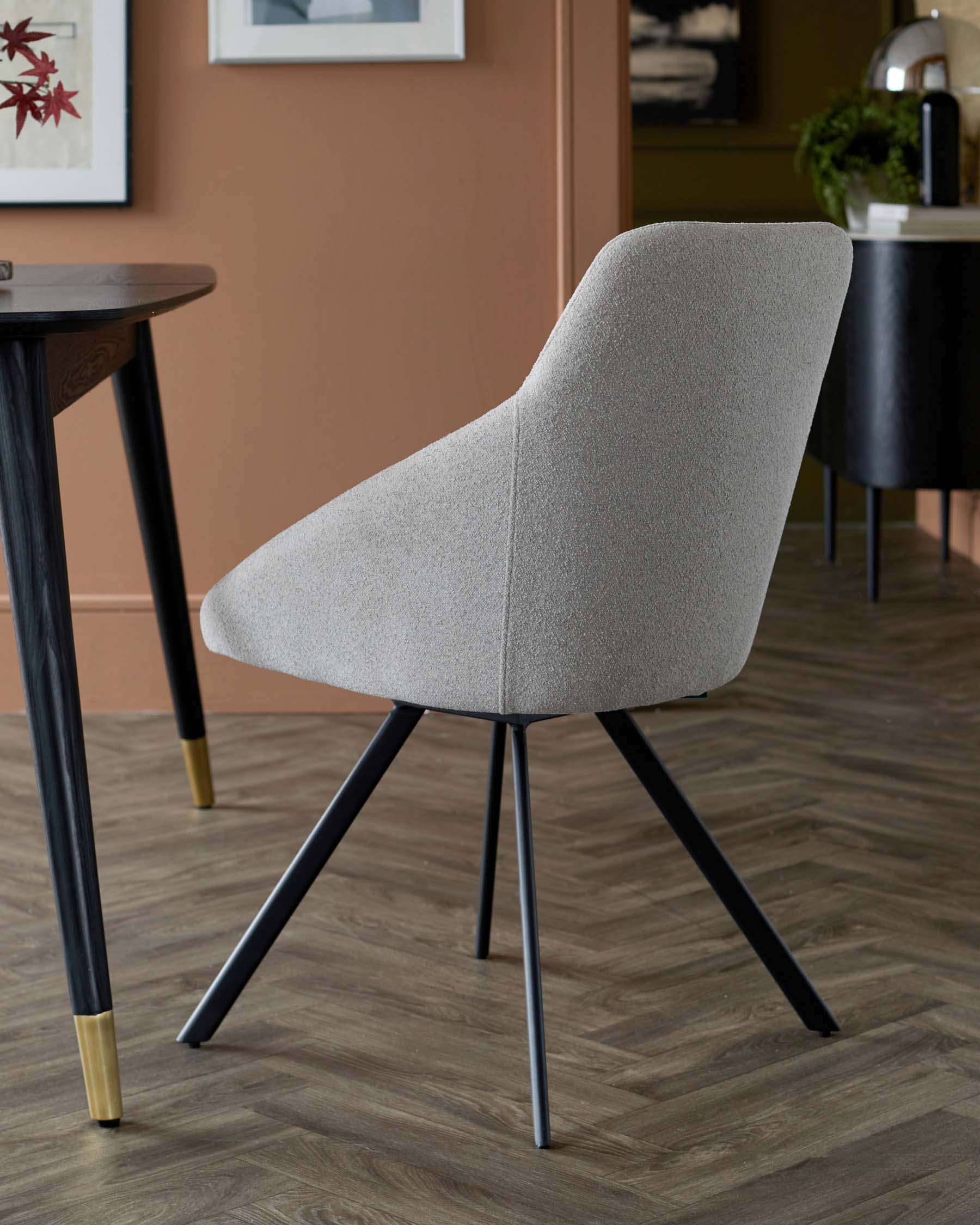 Stylish gray upholstered chair with a sculpted backrest and black metal legs, paired with a wooden table, set in a modern interior.