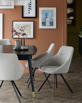 Modern dining set featuring a sleek black table and soft gray chairs with black legs, styled against a warm, earthy wall.