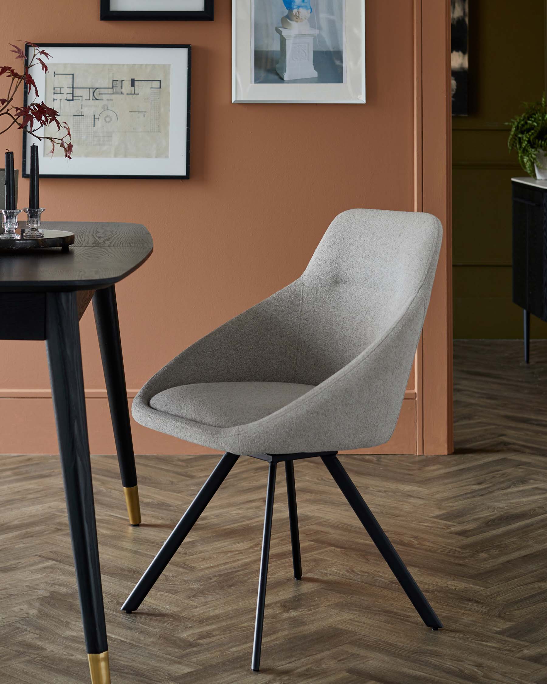 A modern, gray upholstered chair with a curved backrest and black legs, complemented by a dark wooden table, in a stylish setting.