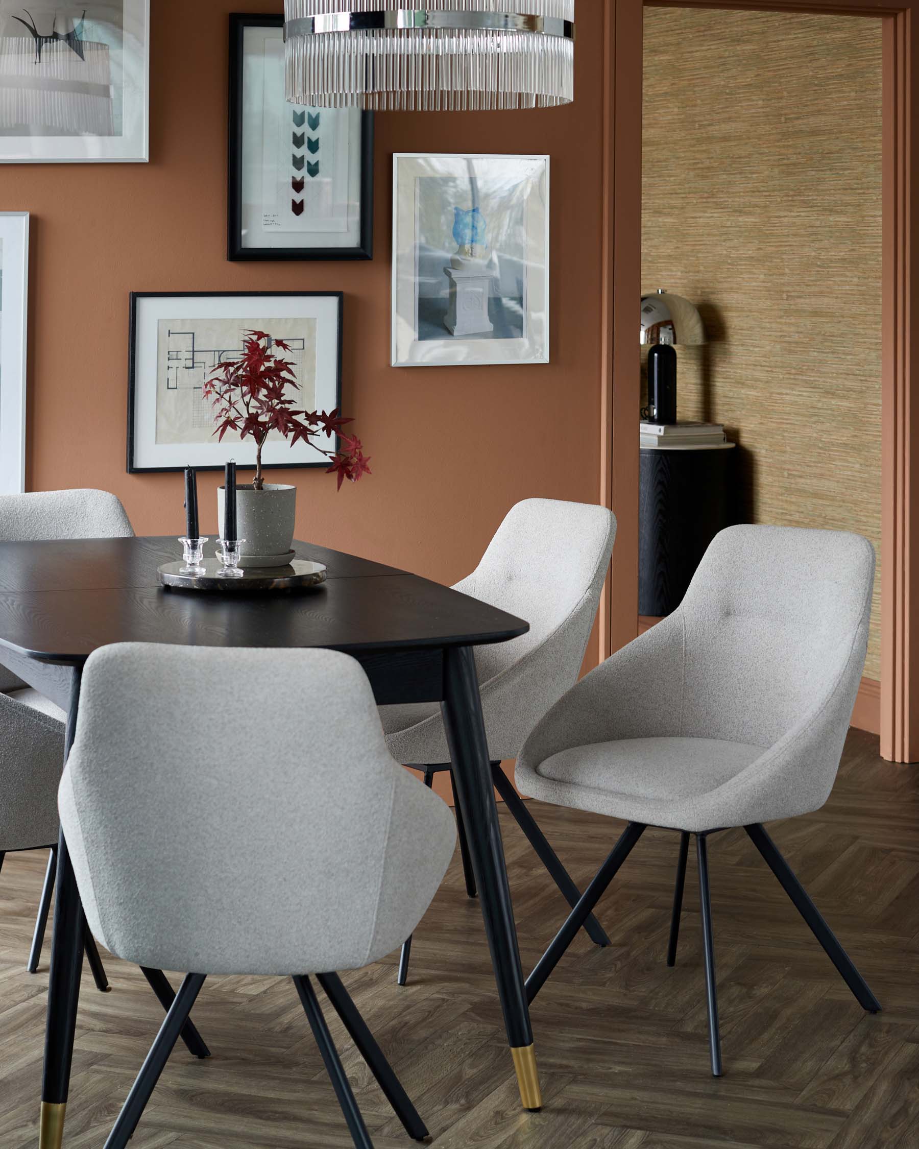 Stylish dining table with four light gray upholstered chairs featuring black legs, accented by gold tips and modern artwork.