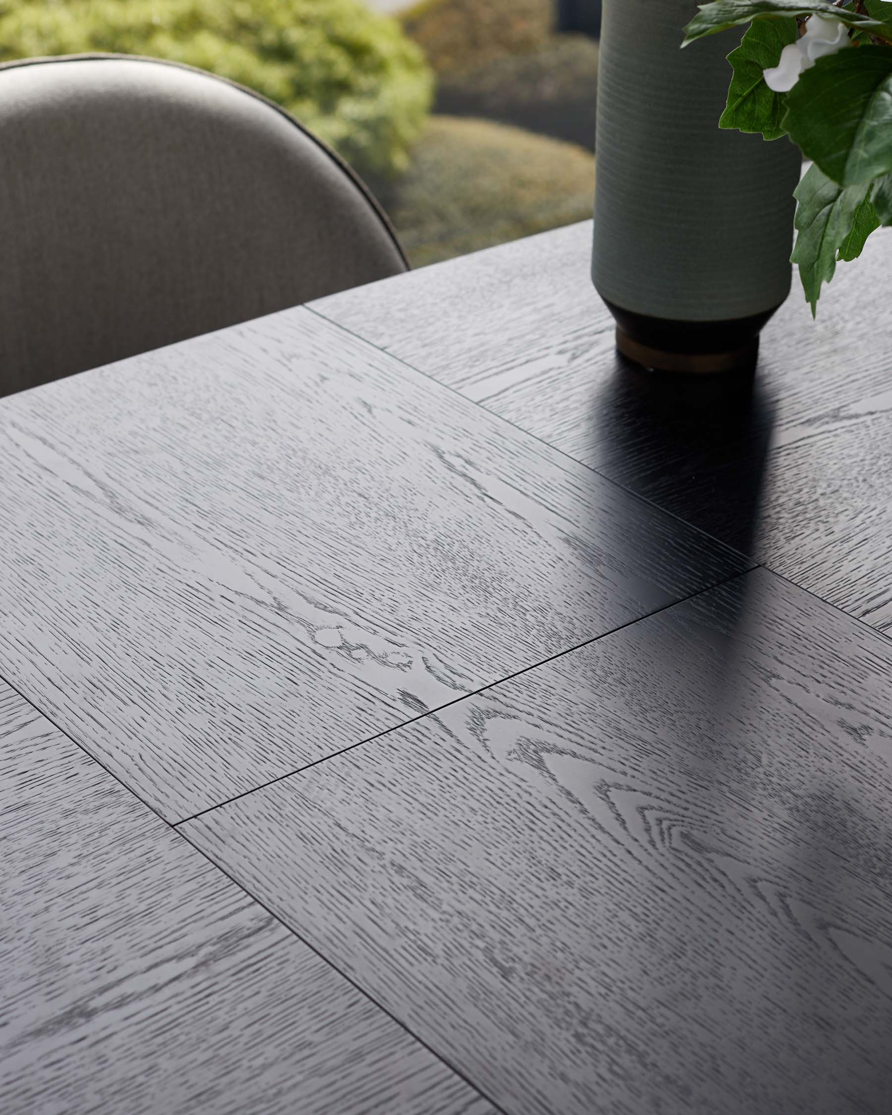 A sleek black wood table with textured surface, complemented by a modern vase and greenery, suggesting elegance and style.