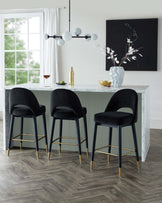 Stylish black velvet bar stools with gold accents set around a marble-topped island, complemented by modern lighting and decor.