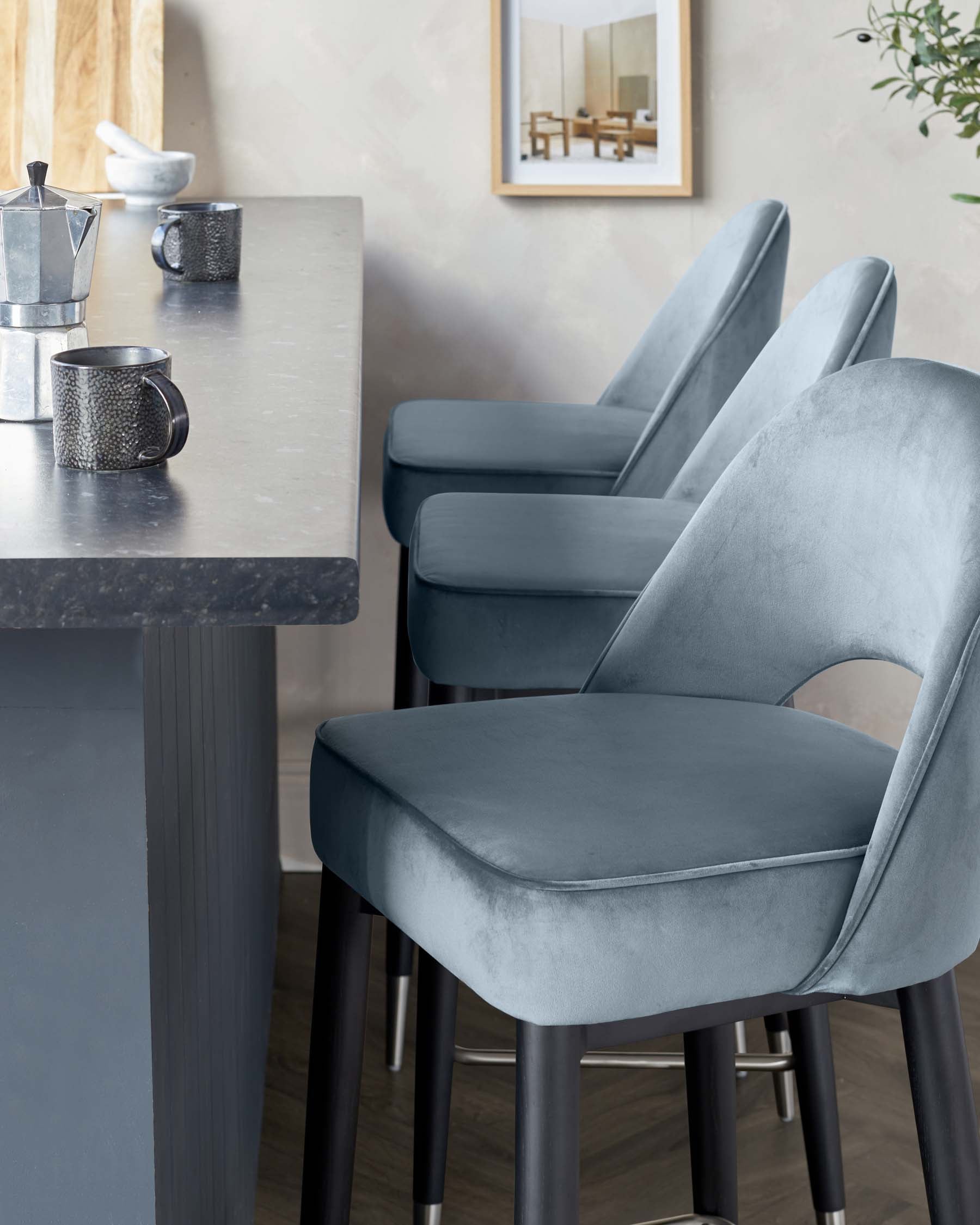 Modern counter-height dining set featuring a stone-grey tabletop on a black sturdy base, complemented by a trio of velvet-upholstered bar stools with backrests, finished in a matching grey tone, each with four black metal legs.