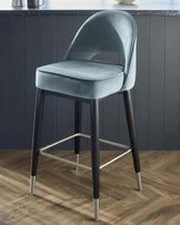 Elegant contemporary bar stool with plush teal velvet upholstery, featuring a curved backrest and a padded seat for comfort. The stool stands on tapered black legs accented with sleek metallic tips and a matching footrest, creating a stylish contrast. Perfect for modern kitchen or bar settings.