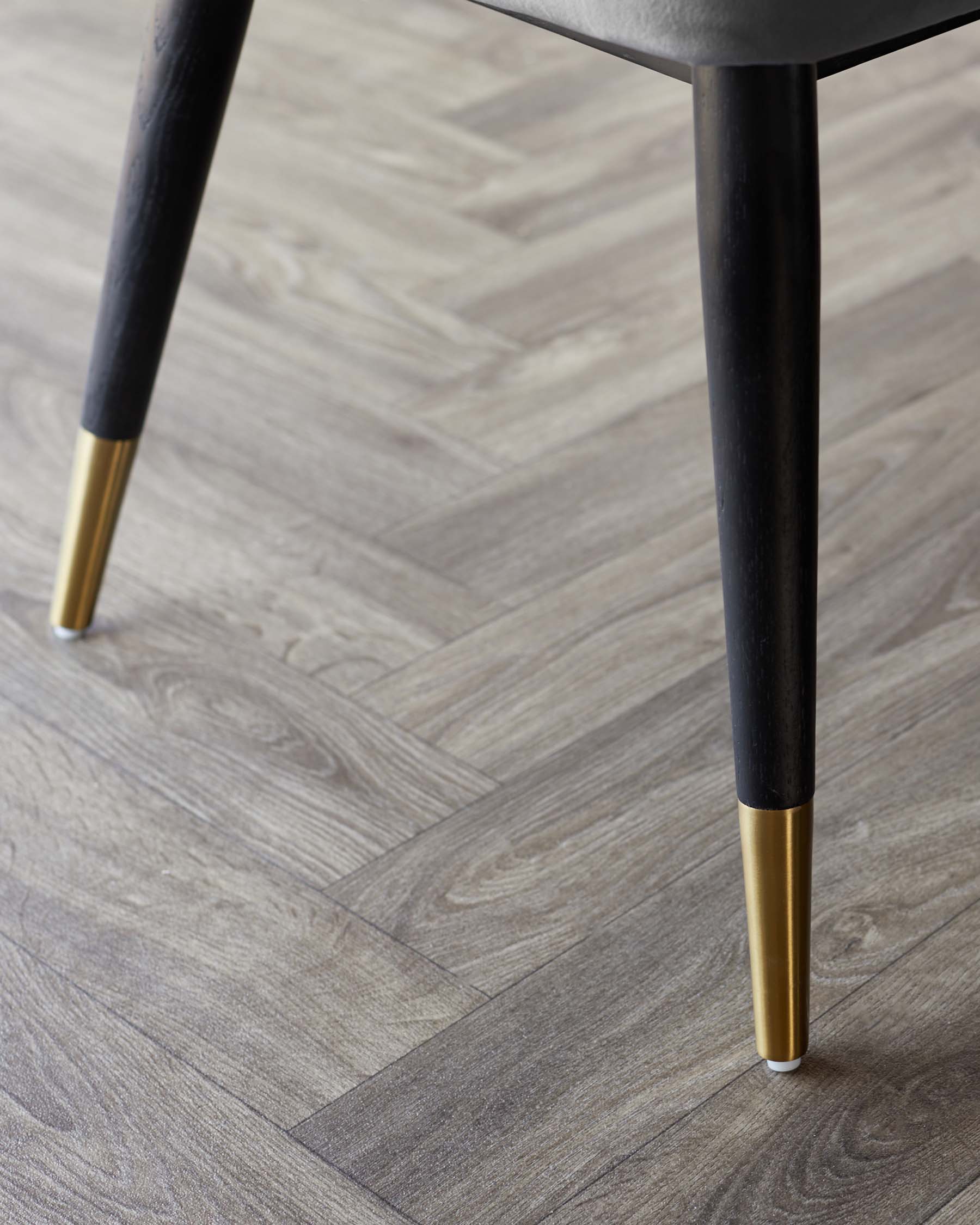 Close-up of a modern table leg with black finish and gold detailing on a herringbone wood floor.