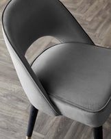 Elegant modern chair with a smooth, curved backrest and cushioned seat upholstered in grey fabric, featuring dark wooden legs with metallic gold accents. The chair's design offers a sleek, contemporary look suitable for both office and home interiors.