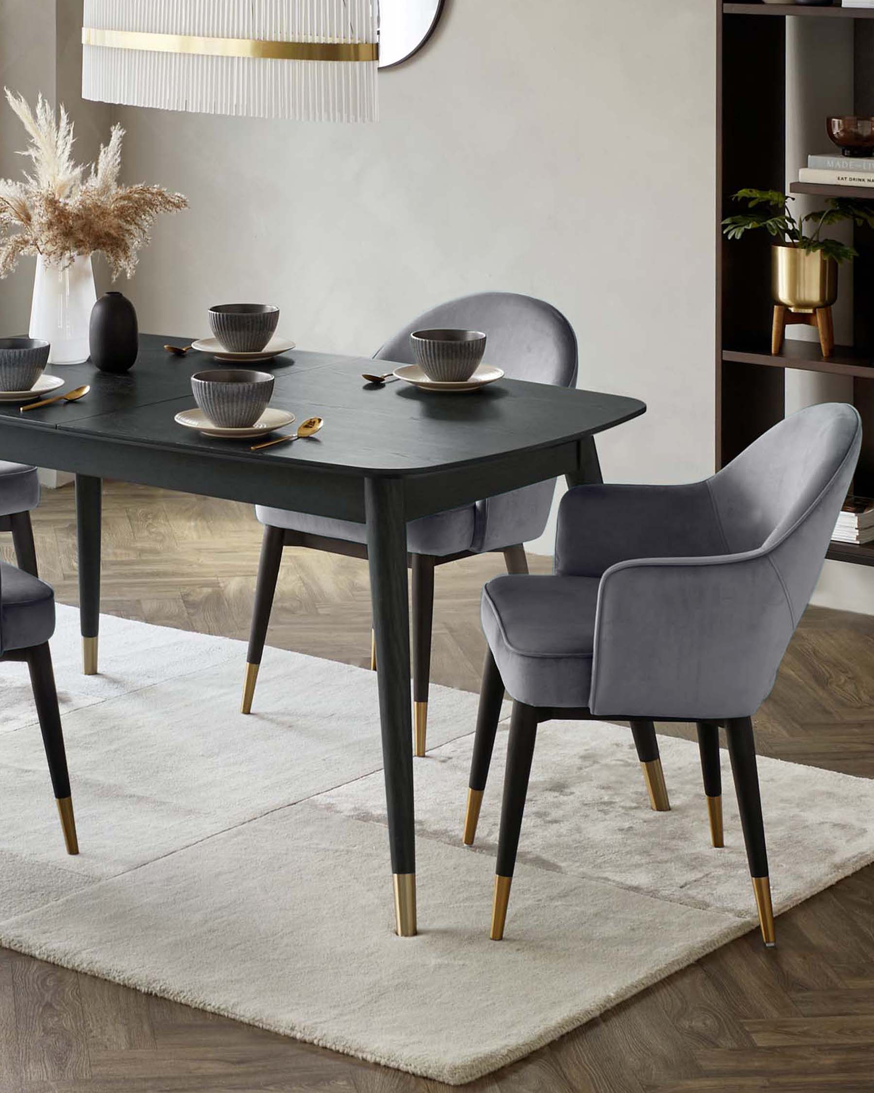 Elegant dining table with dark finish, paired with sleek grey velvet chairs featuring gold-tipped legs, set on a soft rug.