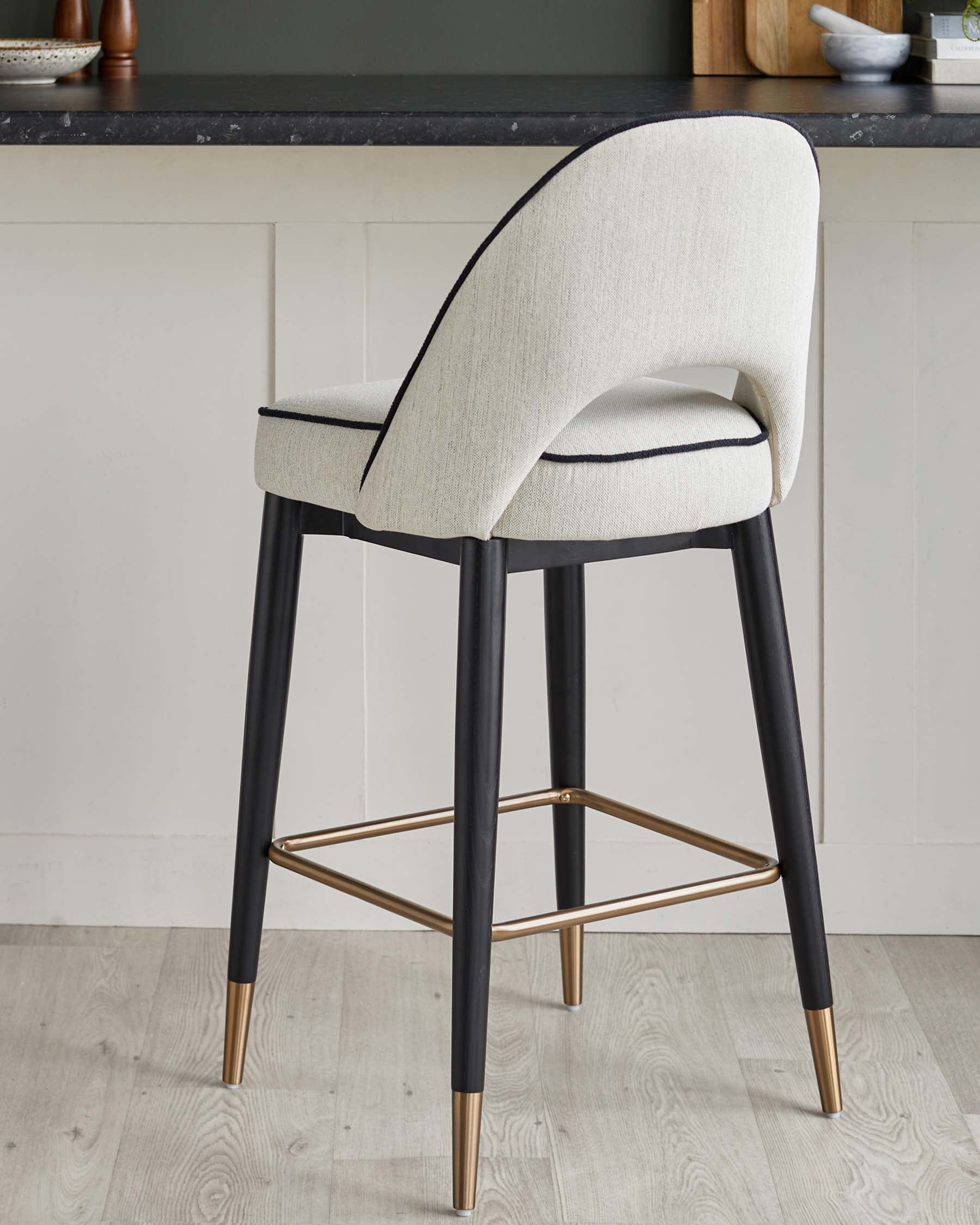 Stylish high stool featuring a cream fabric seat with black trim, slender black legs, and gold-toned feet for a modern touch.