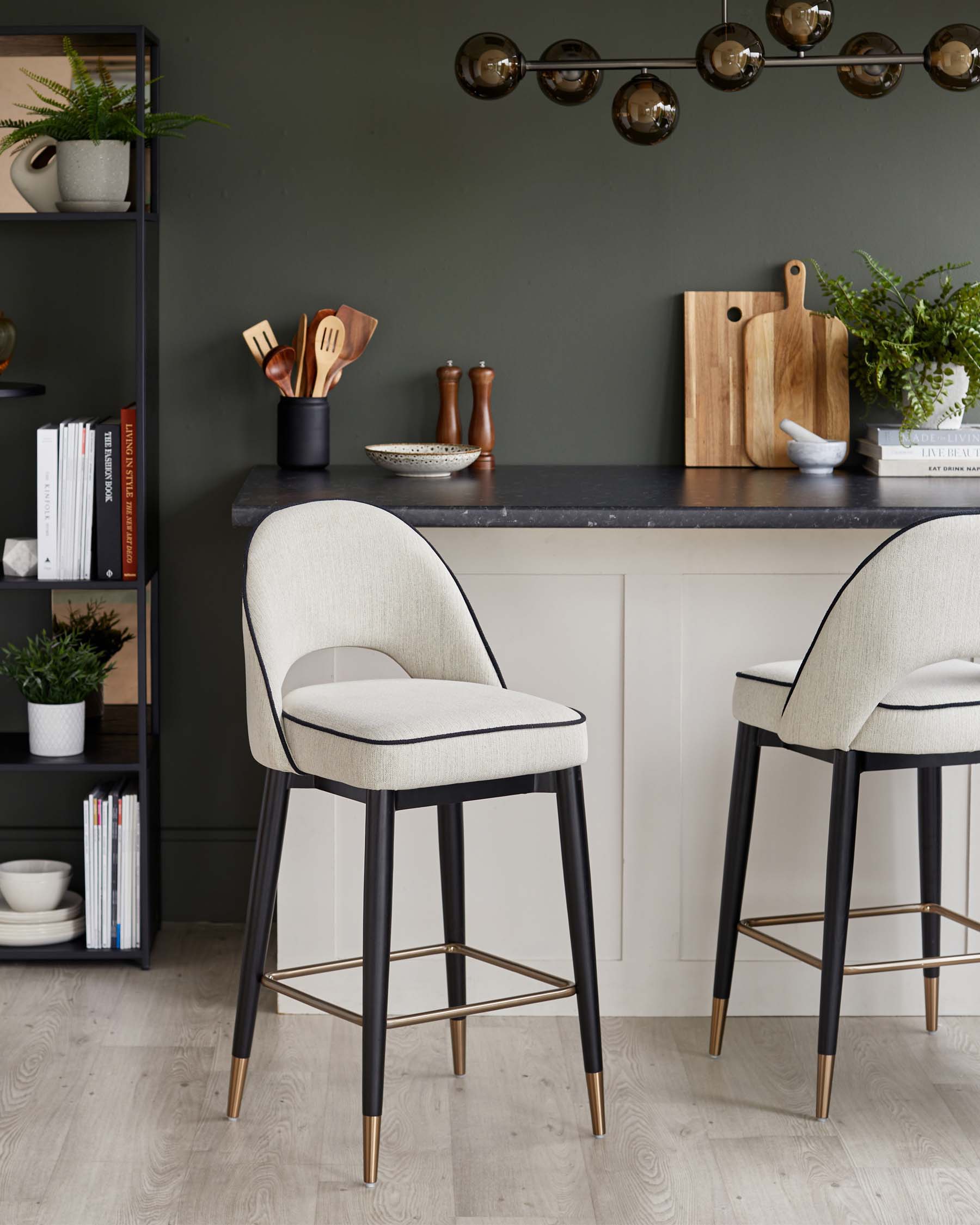 Two modern bar stools with cream upholstery and black legs, accented with gold tips, beside a stylish kitchen counter.