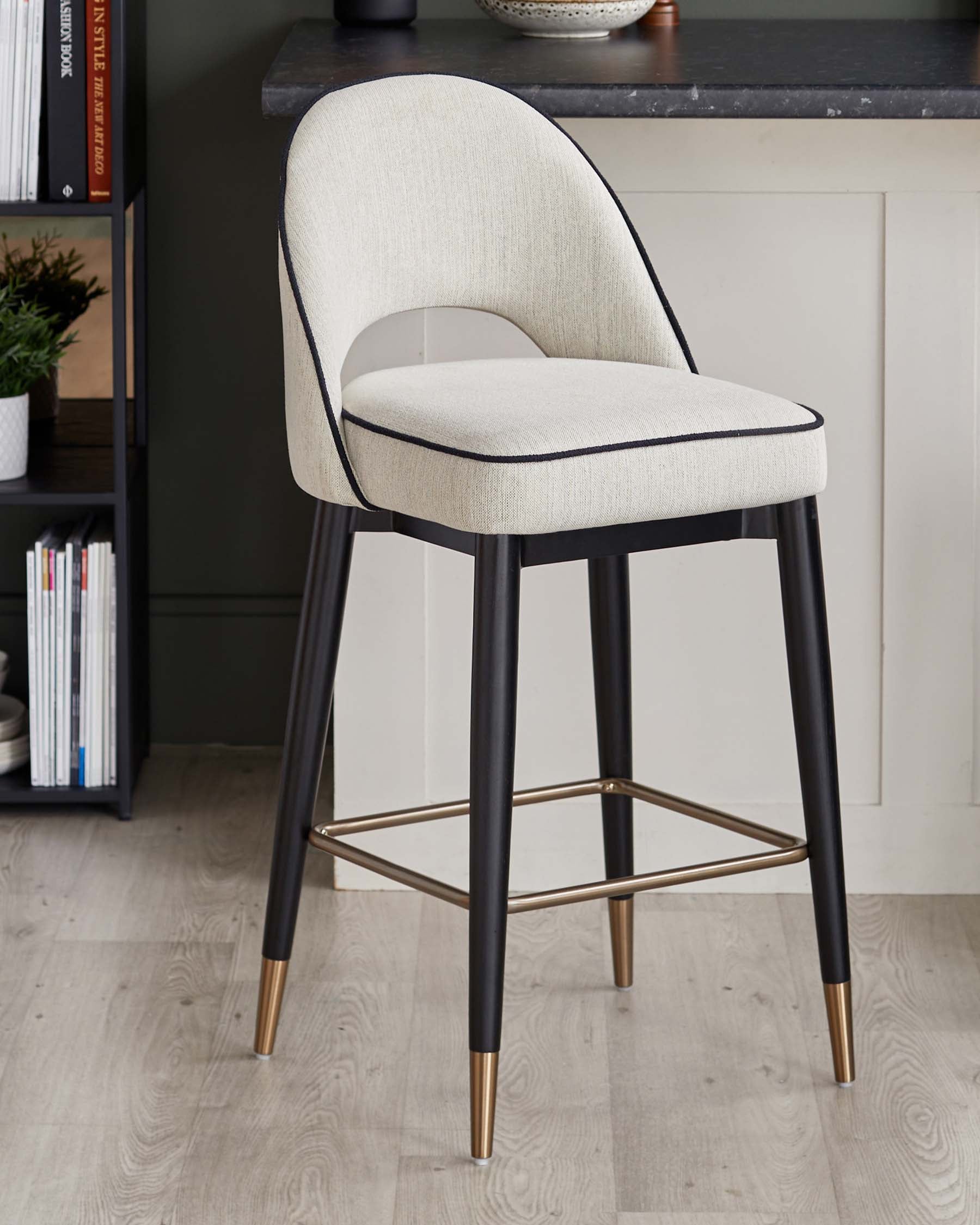 Stylish barstool with a padded cream seat, black legs, and gold accents, perfect for modern dining spaces.